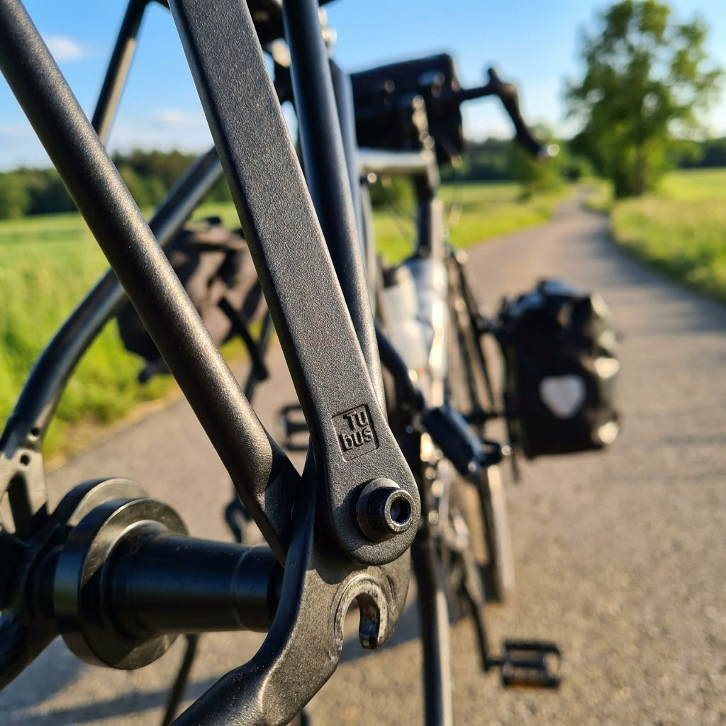 Tubus Rundstrebe Alu 350mm schwarz am Fahrrad-Gepäckträger auf sonnigem Landweg.