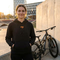 Frau trägt schwarzen FOX Logo Damen Hoodie (Größe L) neben Mountainbike. Ideal für Radsport-Fans.