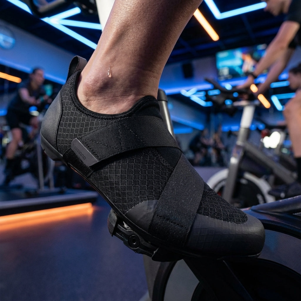 SHIMANO IC100 schwarzer Indoor-Fahrradschuh am Fuß auf Pedal, Schweiß am Knöchel, im Spinning-Kurs.