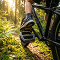 XLC Kinder-/Jugendpedal PD-K15 schwarz/schwarz mit Wassertropfen am Fahrrad im sonnigen Wald.