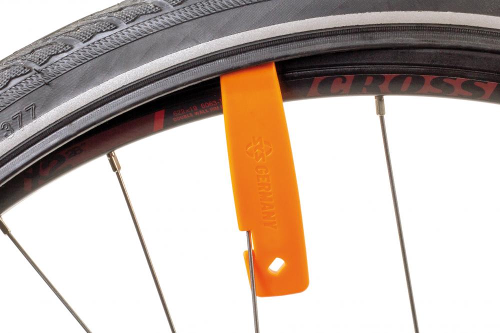 Orangefarbener SKS Reifenheber beim Reifenwechsel an einer Fahrradfelge, an einer Speiche fixiert.