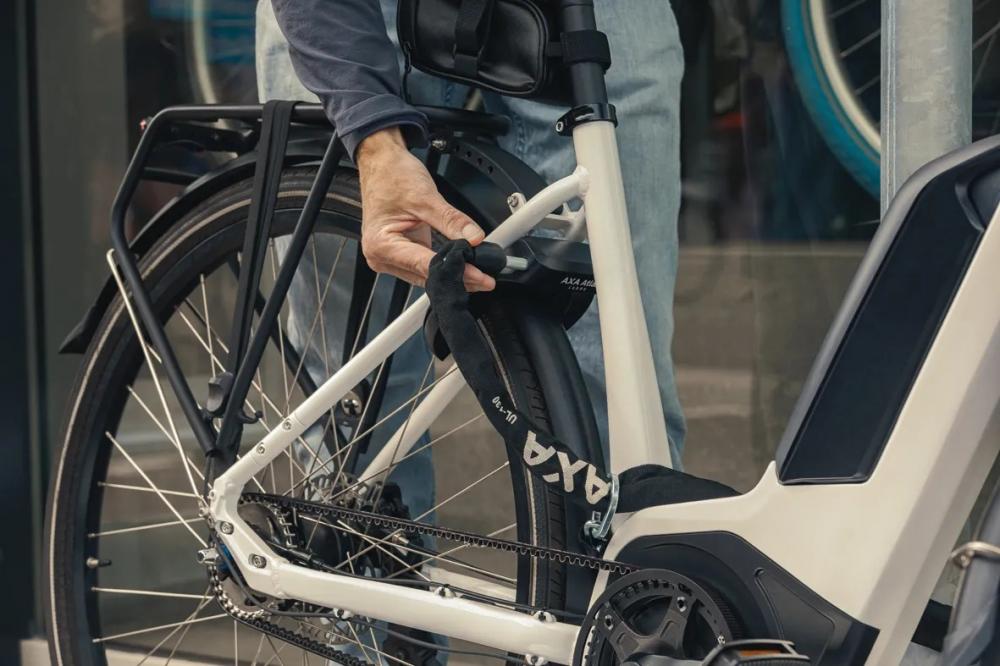 Person sichert weißes E-Bike mit AXA Rahmenschloss Atlas und Kette für extra starken Diebstahlschutz.