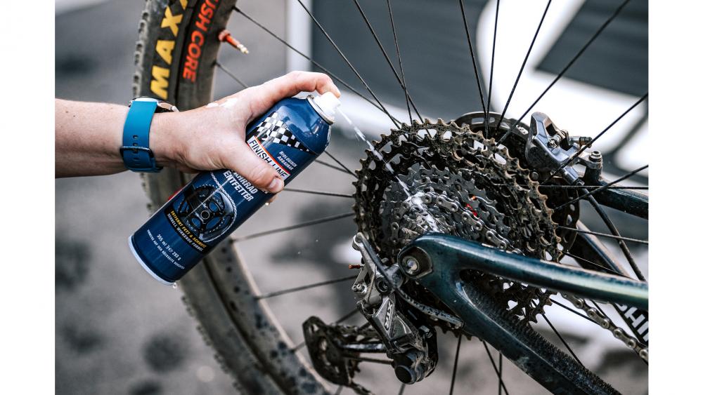 Hand sprüht Finish Line EcoTech Fahrradreiniger auf verschmutzte Kette und Kassette eines Mountainbikes. Starker, biologische