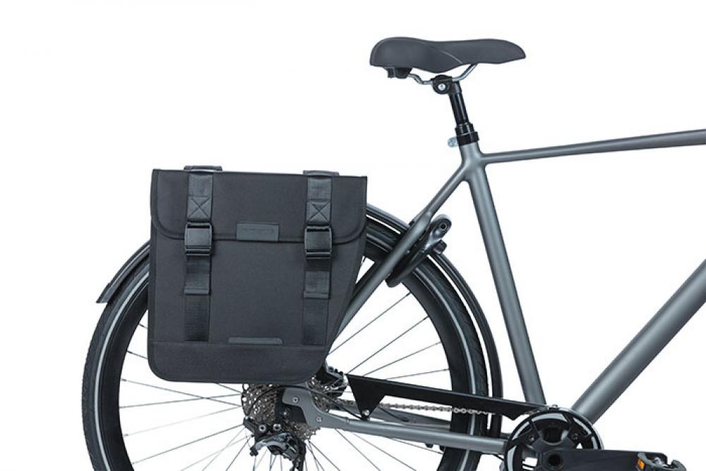 Schwarze Basil Doppeltasche Tour 28 Liter montiert am Gepäckträger eines grauen Fahrrads.