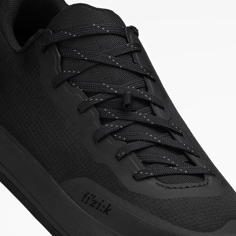 Schwarzer FIZIK Gravita Versor Flat MTB-Schuh mit Ripstop-Obermaterial und reflektierenden Schnürsenkeln für Flatpedale.