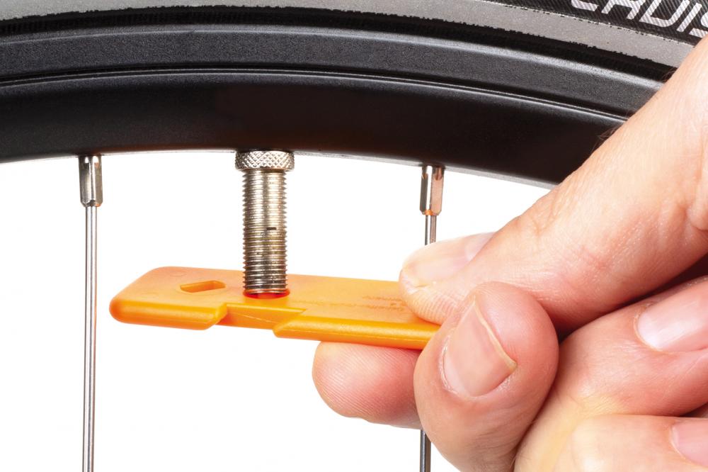 Hand setzt orangefarbenen SKS Reifenheber aus robustem Kunststoff am Fahrradventil für den Reifenwechsel an.