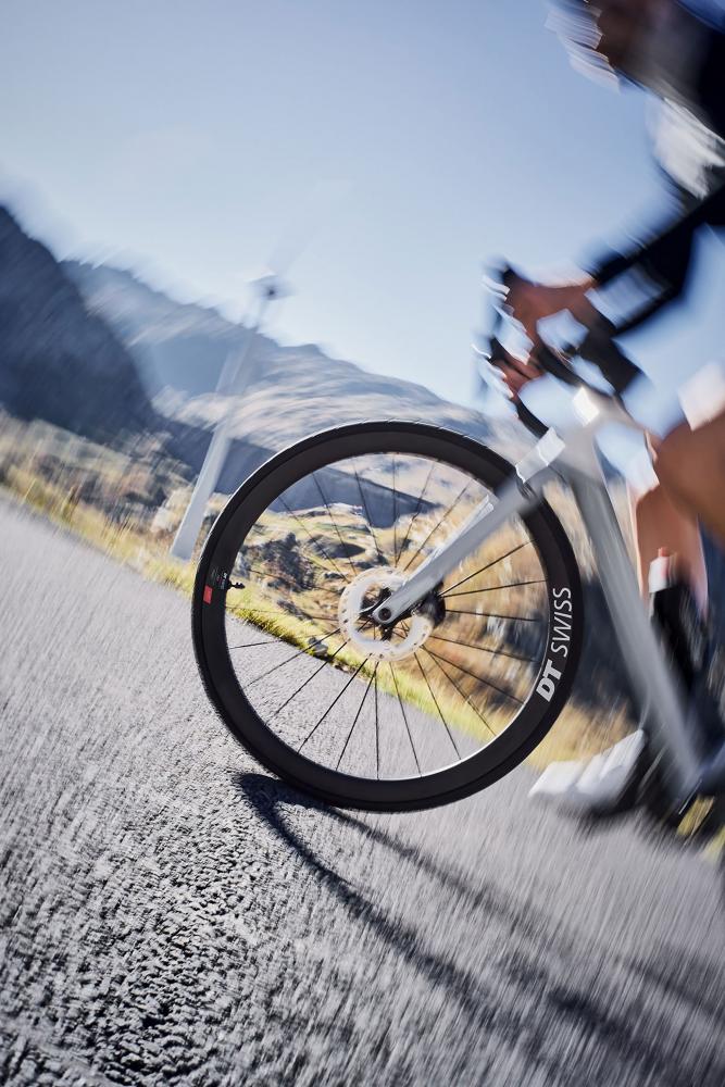 Leichtes DT Swiss ARC 1100 Dicut Disc Aero-Carbonlaufrad schwarz an Radfahrer auf Bergstraße.