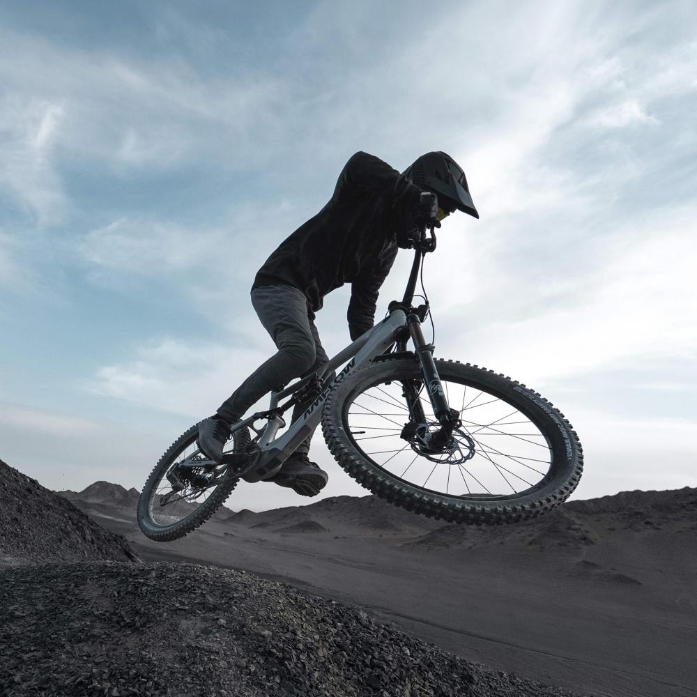 Amflow PX Carbon E-Mountainbike springt mit Fahrer über Felsen, bewölkter Himmel.