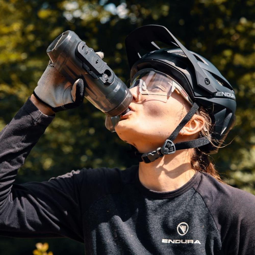 Fidlock TWIST Bottle 590 ml: Radfahrerin trinkt aus ergonomischer, auslaufsicherer Trinkflasche mit magnetischer Bike Base.