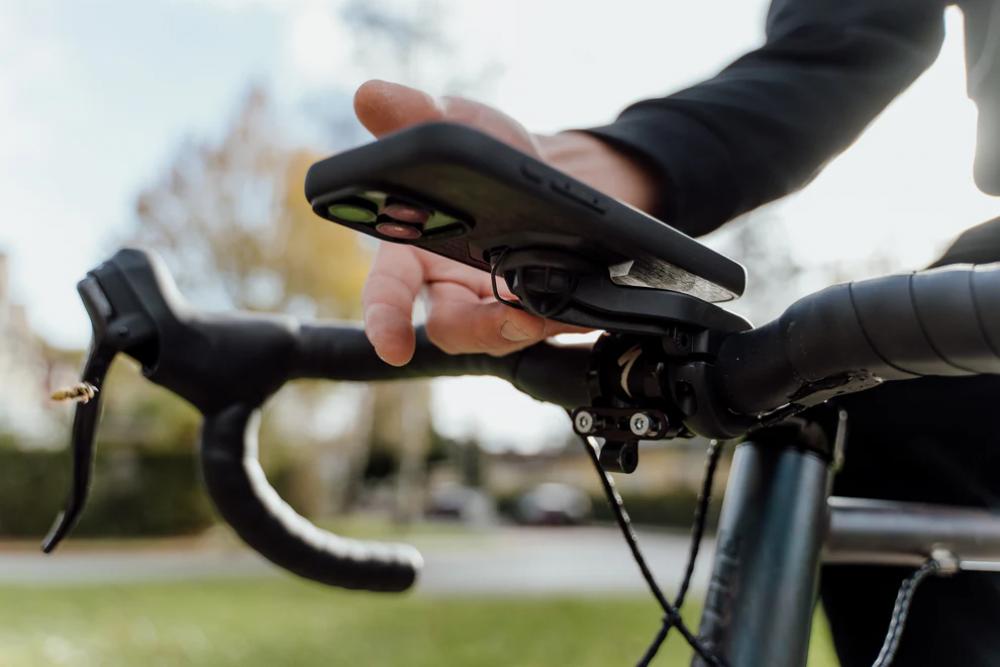 FESCHD Smartphonehalter Bike Bundle schwarz: Person montiert schwarzes Handy an Fahrrad-Lenkerhalterung mit Adapterplatte.