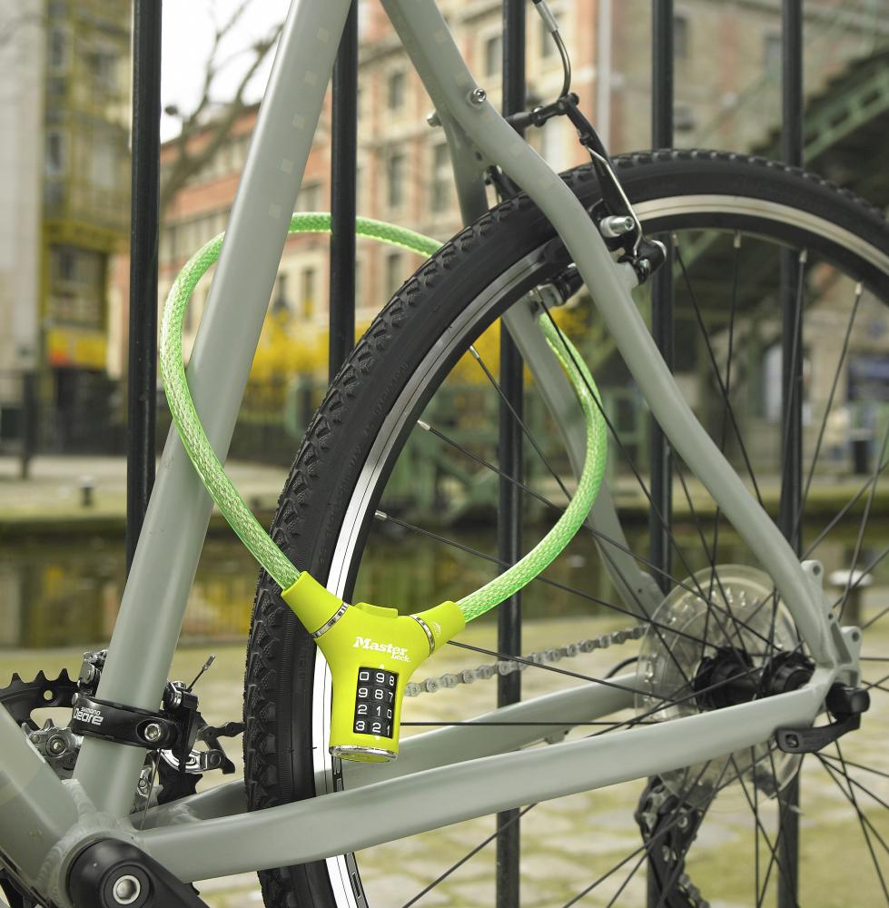 Grünes Master Lock Kabelschloss 8229 mit Zahlencode als Diebstahlschutz für ein Fahrrad am Zaun.