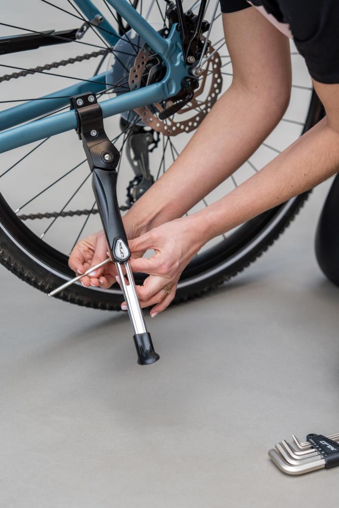 Person montiert schwarzen XLC Hinterbauständer KS-C01 am Fahrrad, verstellbar für 24-28 Zoll.