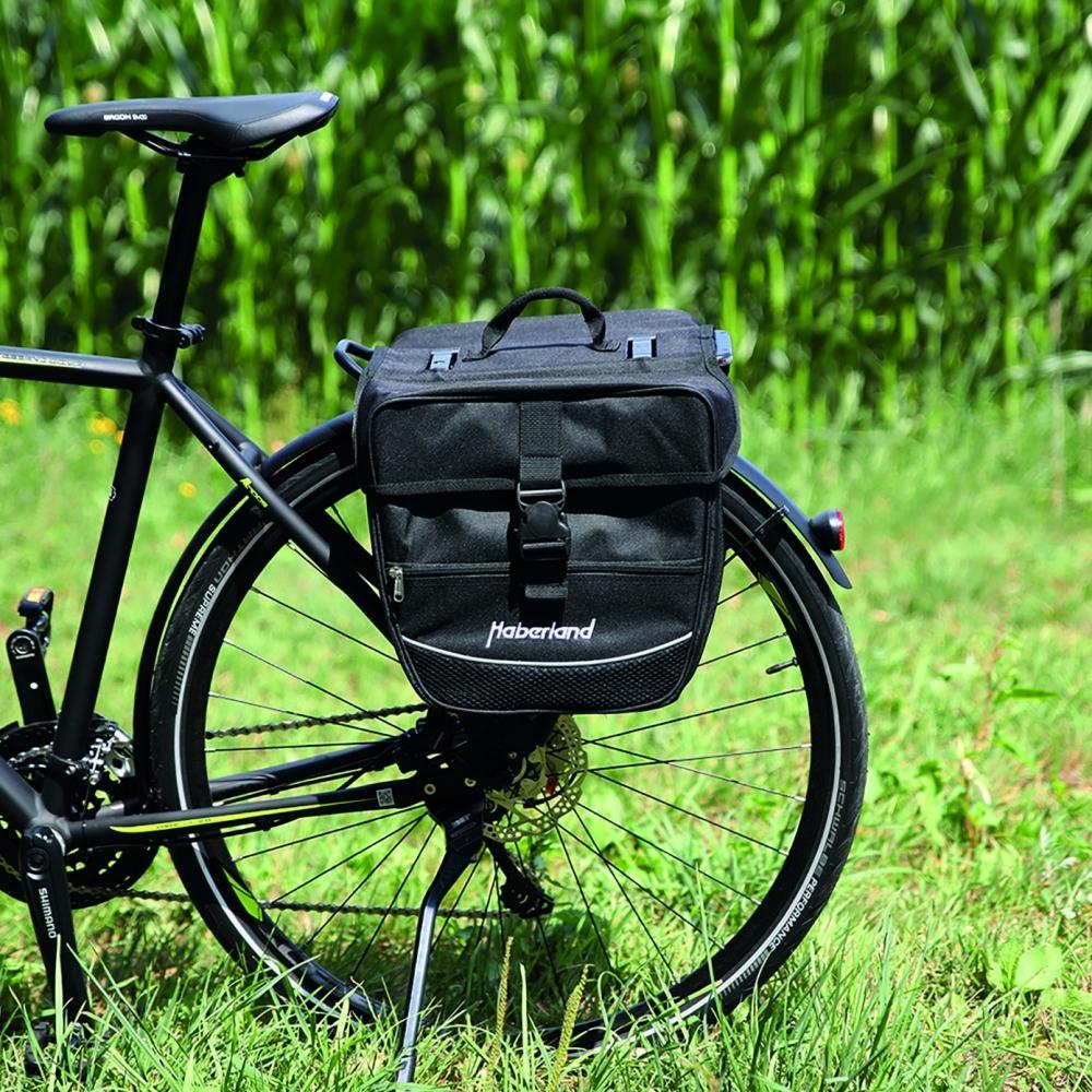 Schwarze Haberland Doppeltasche am Gepäckträger eines Fahrrads im Grünen. Praktische Einsteiger-Fahrradtasche.
