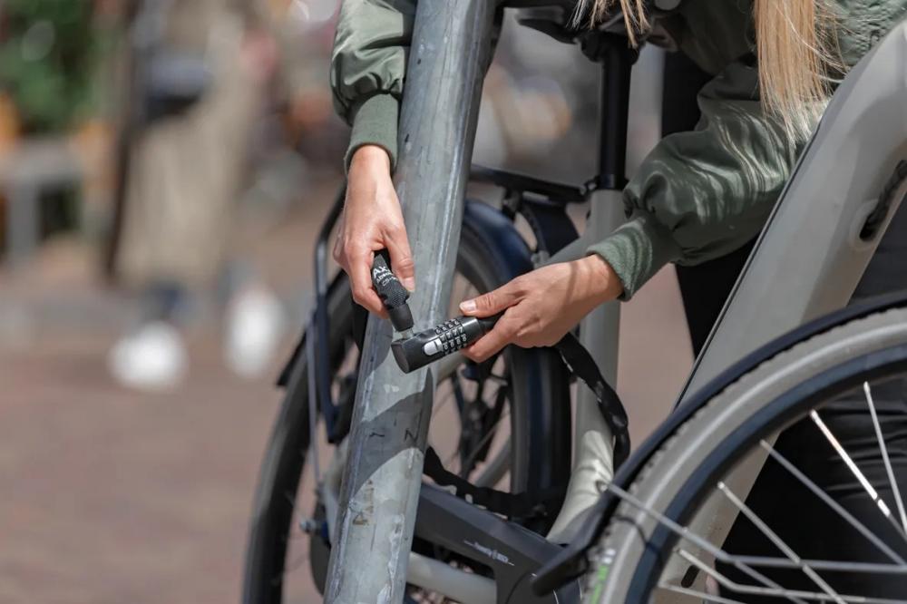 Person schließt Fahrrad mit sicherem AXA Kettenschloss Absolute C5-90 mit Zahlencode.