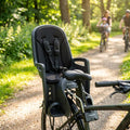 Schwarzer Hamax Zenith Fahrradkindersitz mit Polsterung am Rad, Familie fährt auf Waldweg.