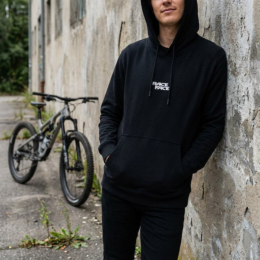Schwarzer Race Face Logo Hoodie an Mann mit Fahrrad im Hintergrund. Bequemer Kapuzenpulli für Biker und Alltag.