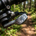 SRAM XX1 Eagle Schalthebel in Lunar/Black am Mountainbike auf einem Waldweg. Präziser Ersatzhebel für Top-Schaltperformance.