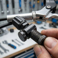 SHIMANO Einstellschraube für Bremszug am Fahrrad, von Hand gehalten, mit Lenker und Werkzeugen im Hintergrund.