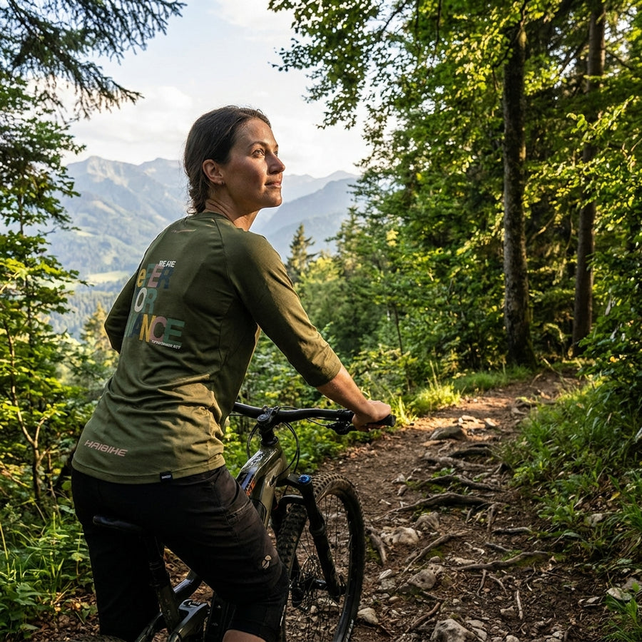 Frau im moosgrünen Haibike Freeride T-Shirt Hochgern by Maloja auf Mountainbike im Wald mit Bergblick.