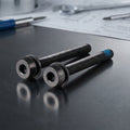 Zwei Campagnolo H11 Scheibenbremsen-Schrauben für hinten auf dunklem Metall, eine mit blauer Spitze.