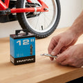 Impac Schlauch 12 Zoll DV 26mm für Kinderfahrrad-Reparatur mit Reifenheber in den Händen.
