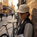 FOX Anniversary Flat 5 Panel Cap beige. Person trägt Kappe, lehnt an Ziegelwand, Fahrrad im Hintergrund.