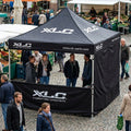 XLC schwarzes 3x3m Faltzelt mit Seitenwand und Logo auf belebtem Marktplatz.