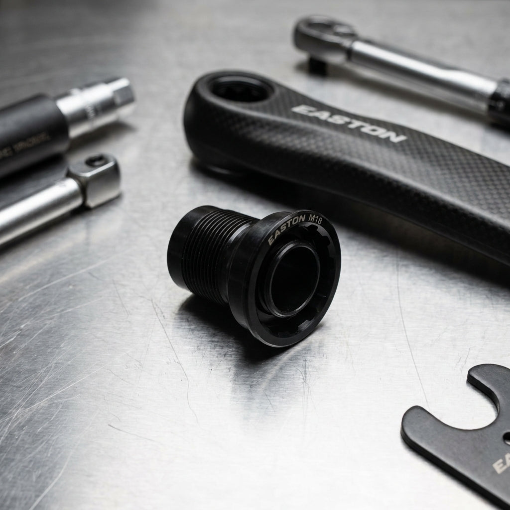 Schwarze Easton M18 Kurbelarmschraube, umgeben von Carbon-Kurbelarm und Montagewerkzeugen auf Metall.