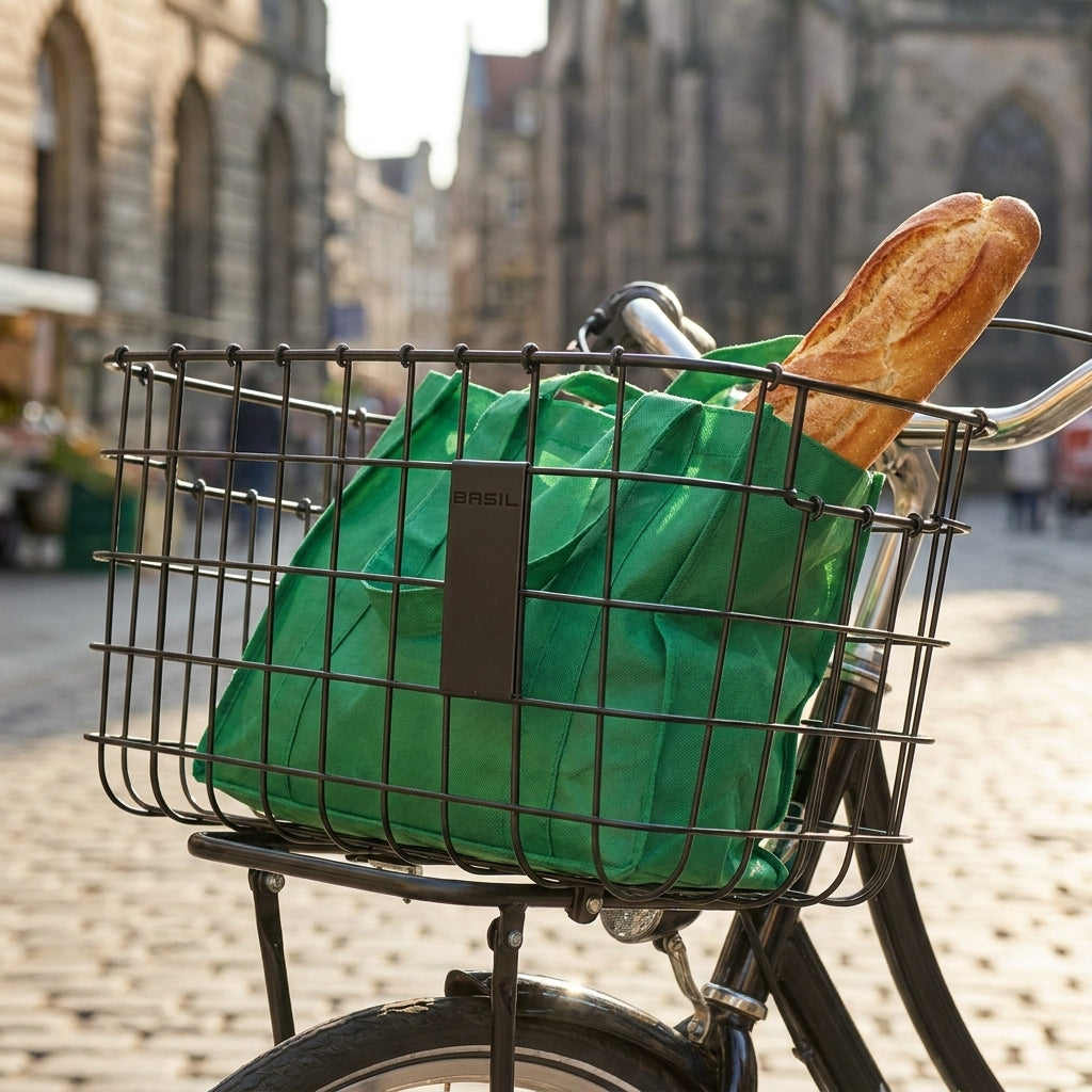 Basil Robin Vorderradkorb schwarz am Fahrrad, gefüllt mit grüner Einkaufstasche und Baguette in der Stadt.
