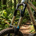 Schmutzige Rockshox Mountainbike Federgabel mit Troy Lee Designs Dekor Kit in Gold und Blau im Wald.