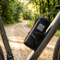 Elite TAKUIN Transportflasche schwarz, wasserdicht, mit grauer Grafik am Fahrrad auf Waldweg.