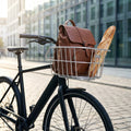 Alufarbener Basil Cento Aluminium Fahrradkorb mit braunem Lederrucksack und Baguette auf schwarzem Rad.