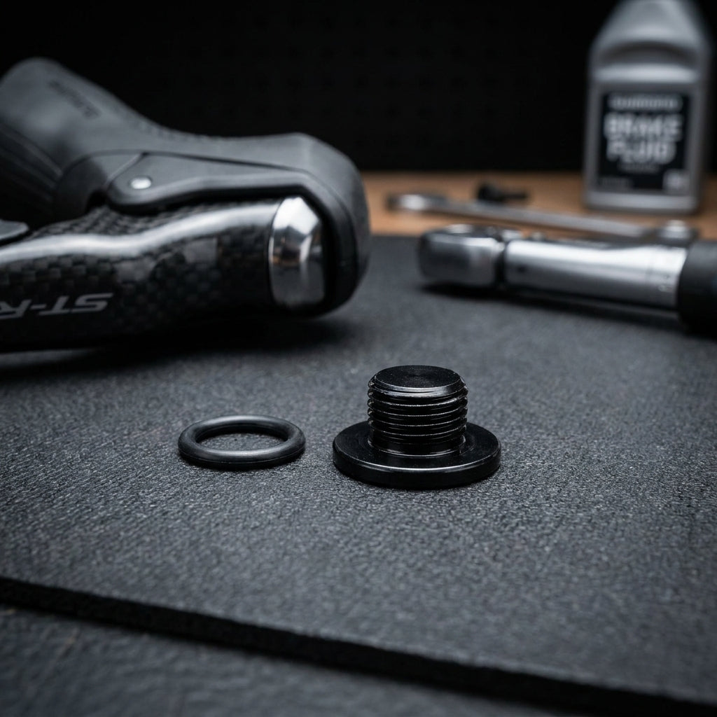 SHIMANO Entlüftungsschraube ST-R9120 und O-Ring für Fahrradbremsen. Im Hintergrund Bremsflüssigkeit und Hebel.