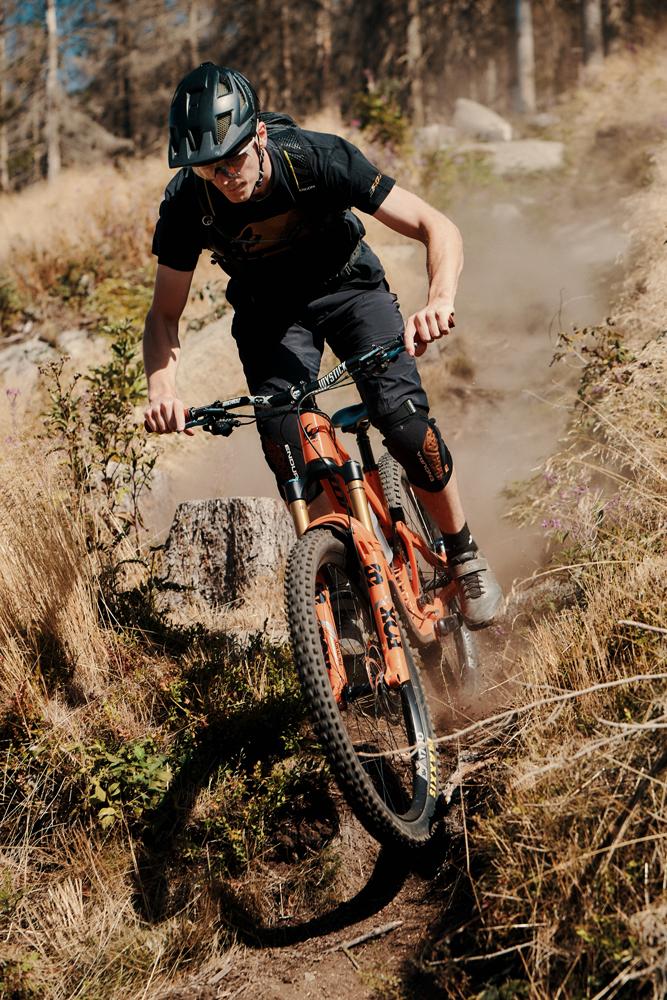Mountainbiker auf orangefarbenem Fahrrad fährt einen staubigen Trail im Wald hinunter.
