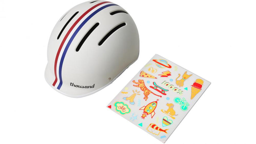 Thousand JR Speedway Crème Kinderfahrradhelm mit roten/blauen Streifen und Blatt voller bunter abnehmbarer Sticker.