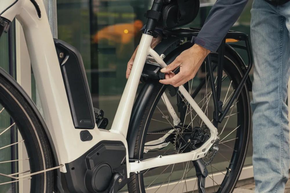 Person befestigt AXA Rahmenschloss Atlas 58 mm an weißem E-Bike für extra starken Diebstahlschutz.