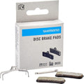 Shimano D03S-RX Resin Scheibenbremsbeläge in Verpackung mit Feder und Splint für leise, kraftvolle Disc-Performance.