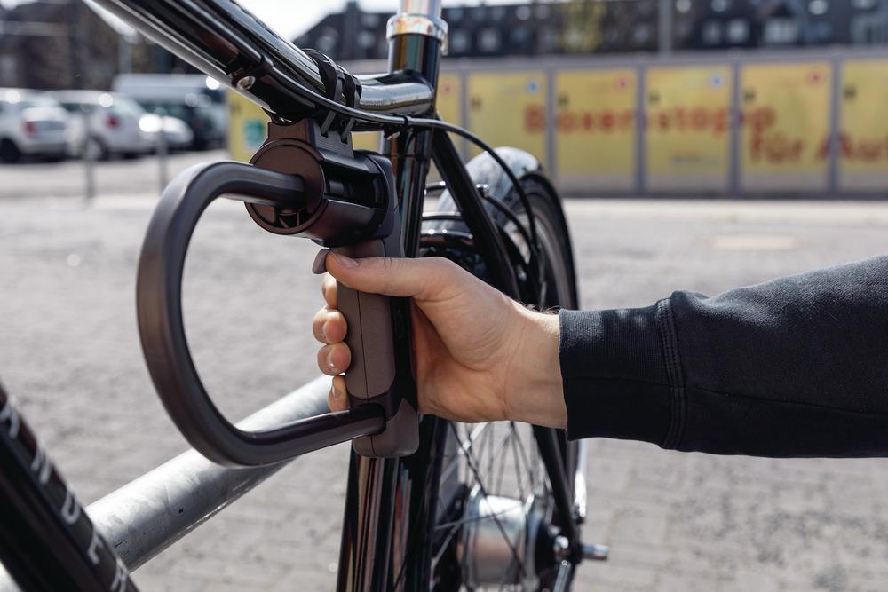 Abus Halter SHB für Bügelschlösser am Fahrradrahmen. Eine Hand hält die Halterung mit dem Bügelschloss.