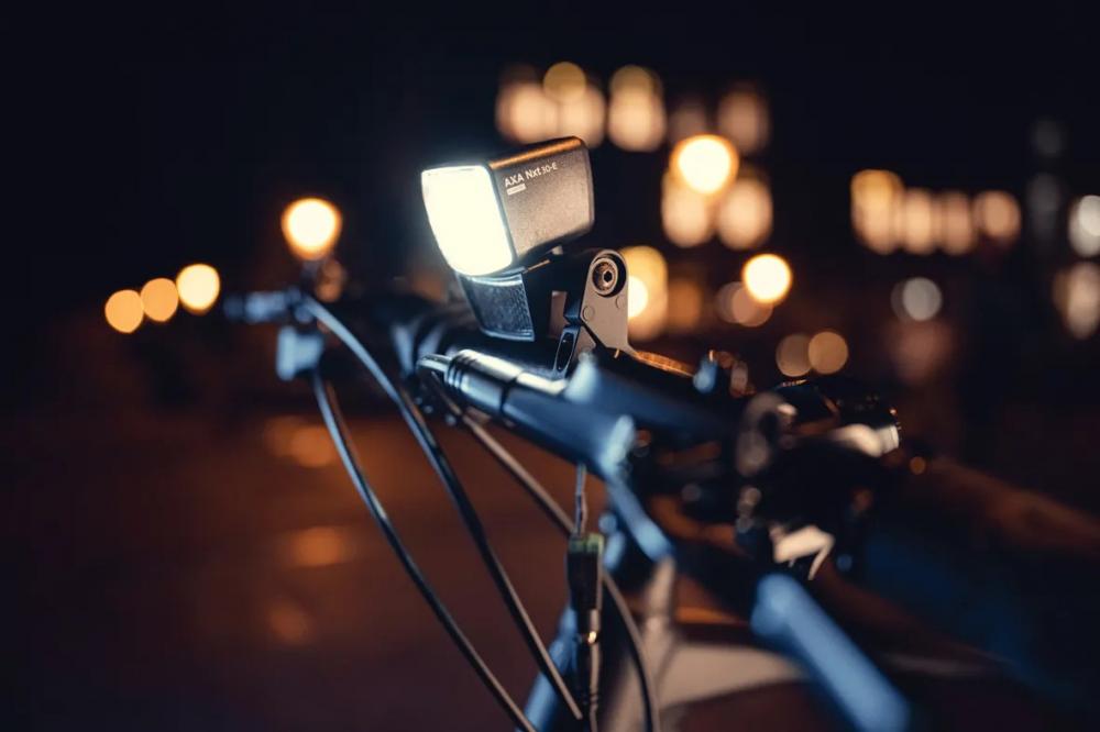 Axa Lenkerhalterung für Scheinwerfer NXT schwarz am Fahrradlenker, nachts mit hellem Licht und Bokeh.