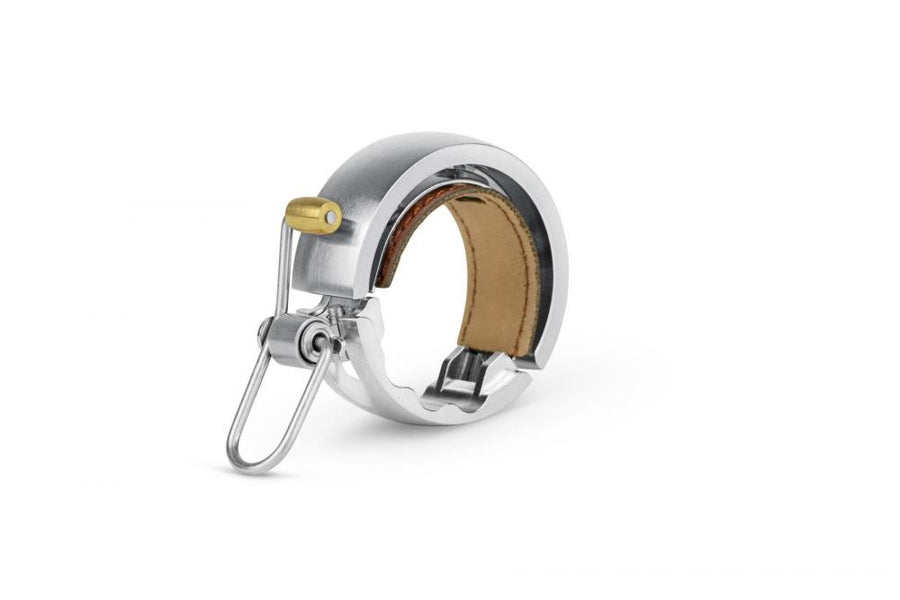 Knog Oi Luxe Fahrradklingel groß silber 23.8-31.8mm, mit Messinghebel und braunem Leder.