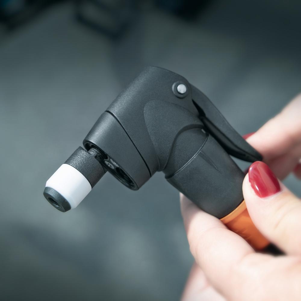 SKS Clik-Valve Adapter für Fahrrad-Pumpenköpfe in Schwarz-Orange, von Hand gehalten, mit weißer Spitze.