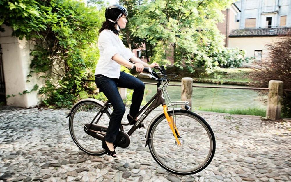 Frau fährt Fahrrad mit Selle Royal Torx Unisex Sattel auf Kopfsteinpflaster am Fluss.