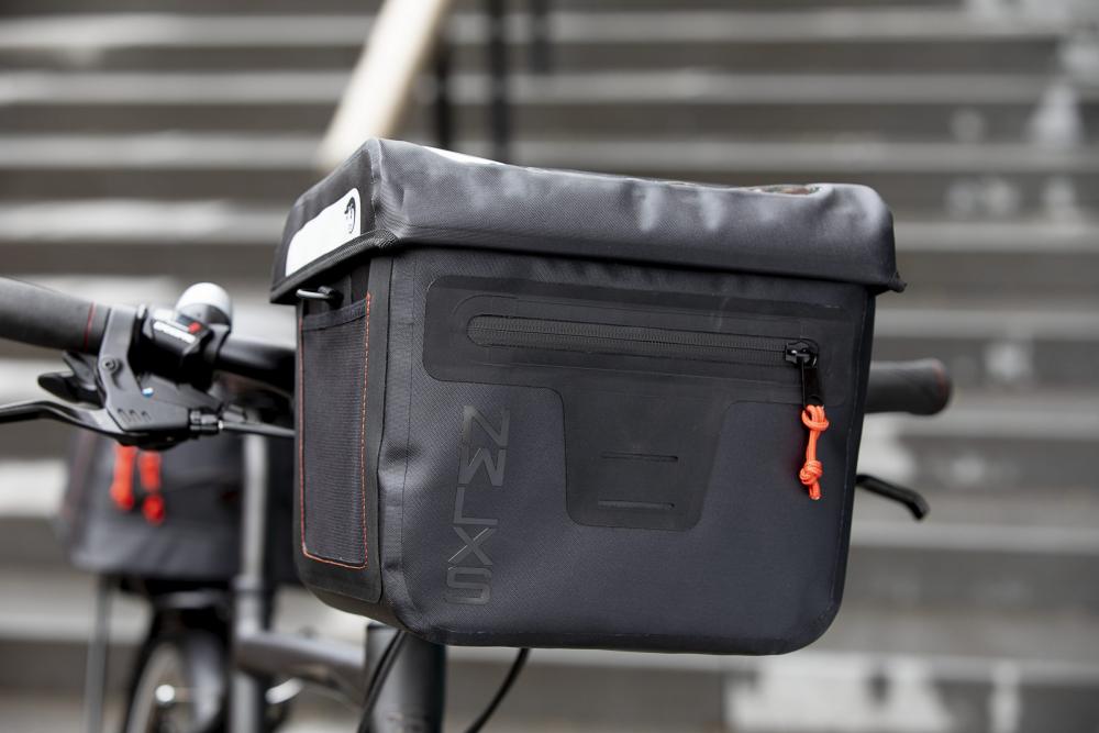 New Looxs Varo Lenkertasche schwarz am Fahrradlenker, mit Fronttasche, NXLS Logo und orangefarbenem Zipper.