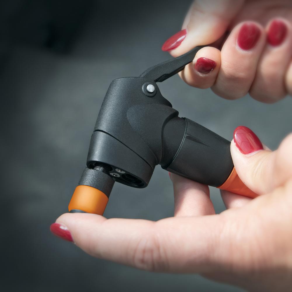 Hände halten SKS Clik-Valve Adapter für Fahrradpumpen, schwarz-orange, für präzisen und sicheren Ventilwechsel.