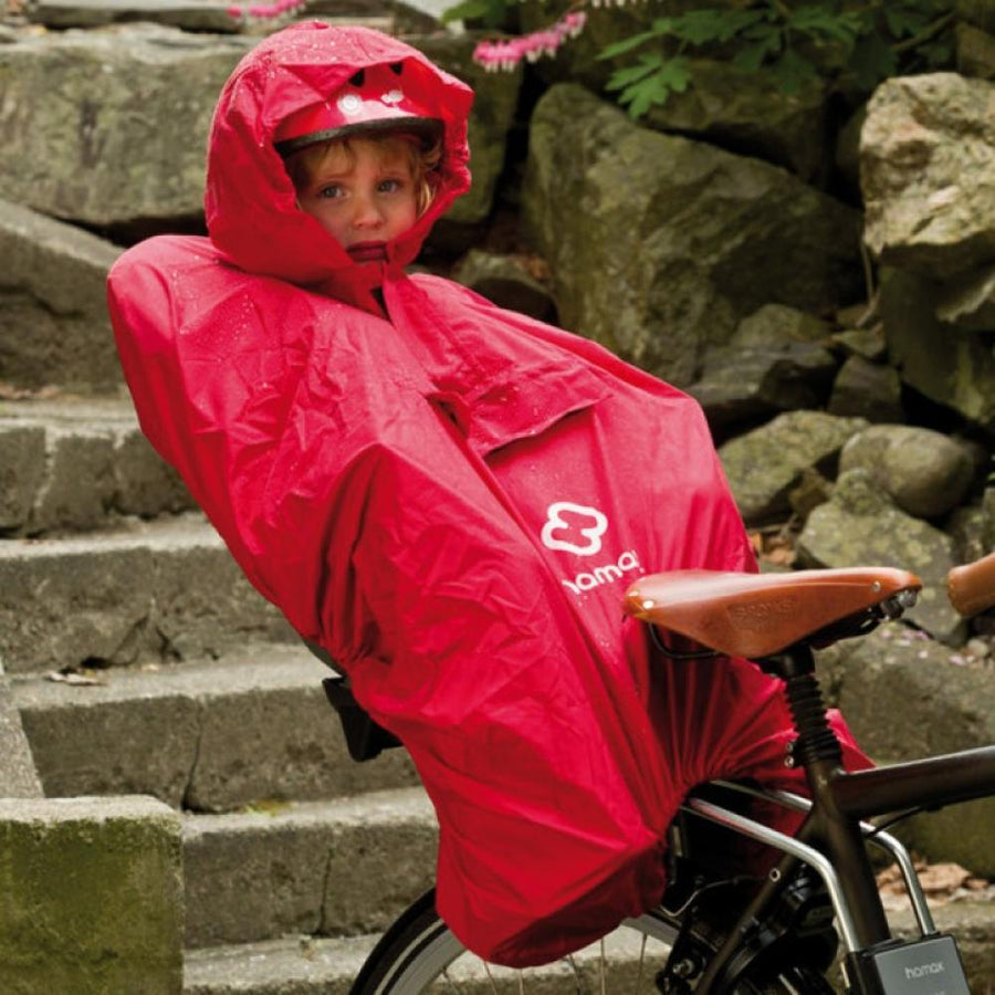 Kind im roten Hamax Regenponcho in Fahrradsitz, geschützt vor Regen.