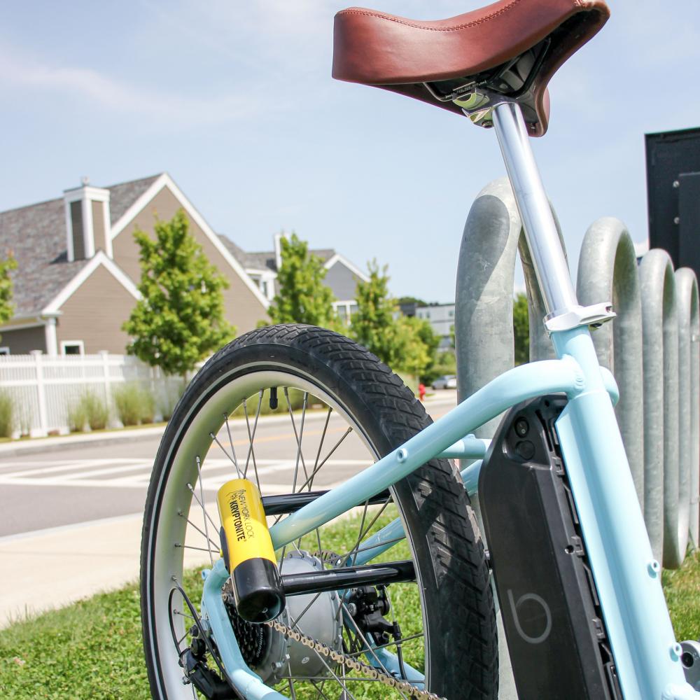 Schwarz-gelbes Kryptonite New York M18-WL Bügelschloss sichert hellblaues E-Bike am Hinterrad. Fahrradschloss.