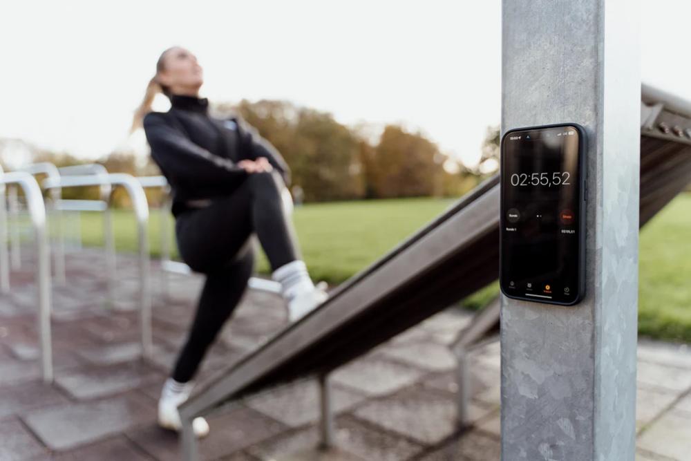 FESCHD Smartphonehalter Bike Bundle schwarz an Metallpfahl, Handy mit Stoppuhr, Frau dehnt sich draußen.