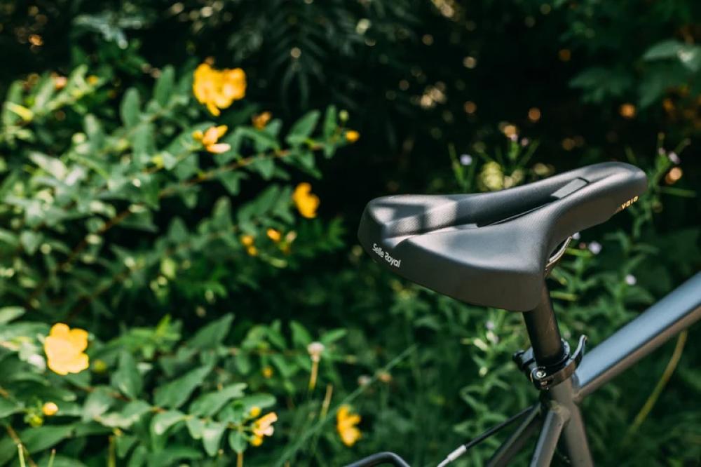 Selle Royal Vaia Moderate Unisex Fahrradsattel an grauem Fahrradrahmen vor grünem Hintergrund mit gelben Blumen.